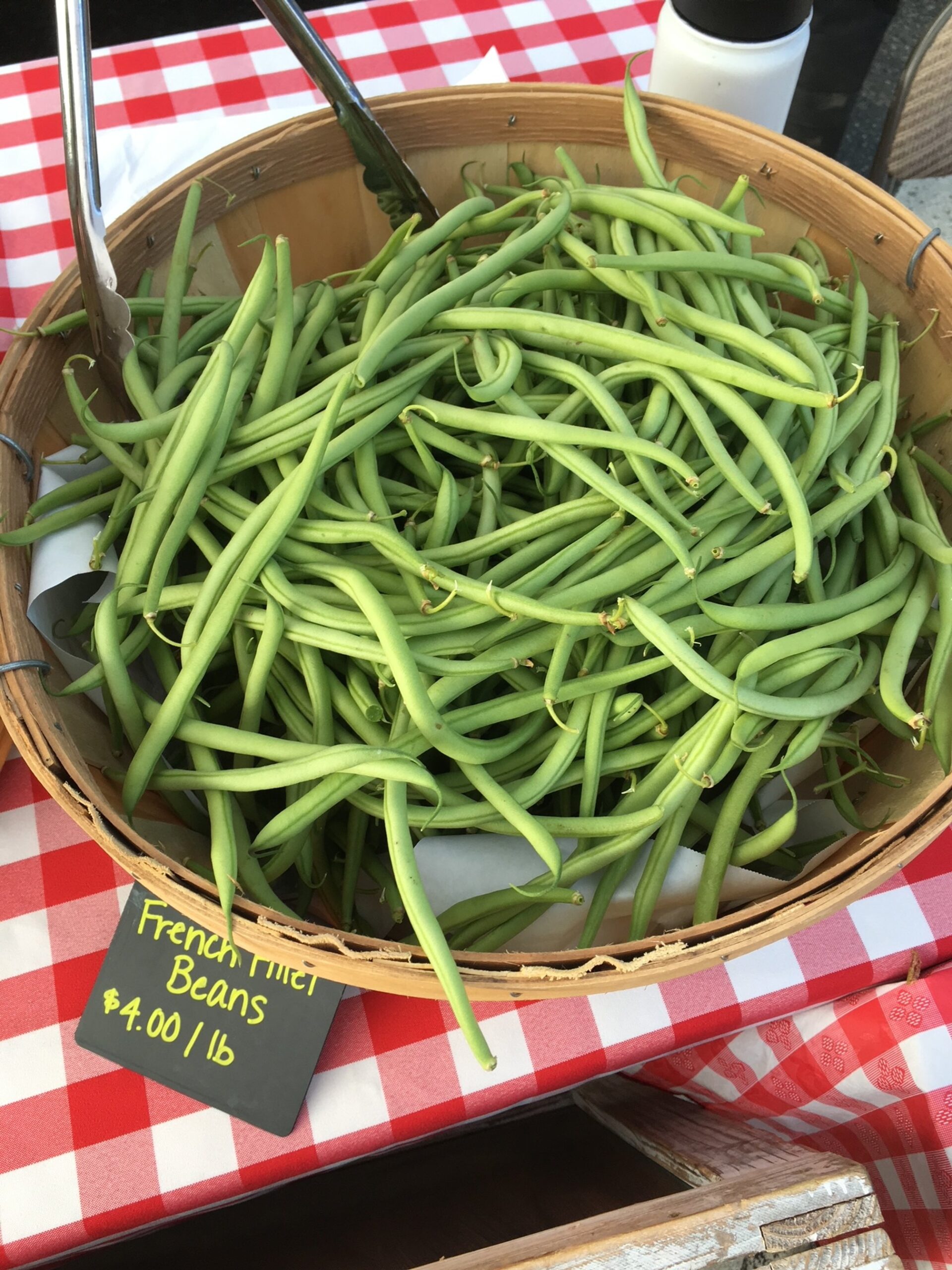 Basket of fresh French filet beans for sale at a market, priced at $4.00 per pound, with a red and white checkered tablecloth in the background.
